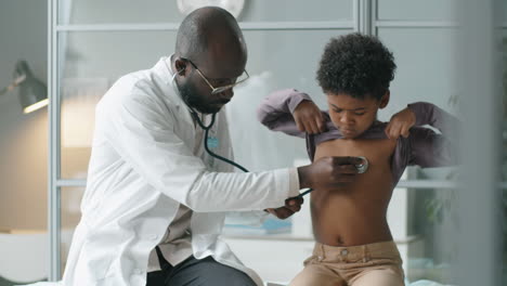 Afroamerikanischer-Arzt,-Der-Einem-Kleinen-Jungen-Eine-ärztliche-Untersuchung-Durchführt